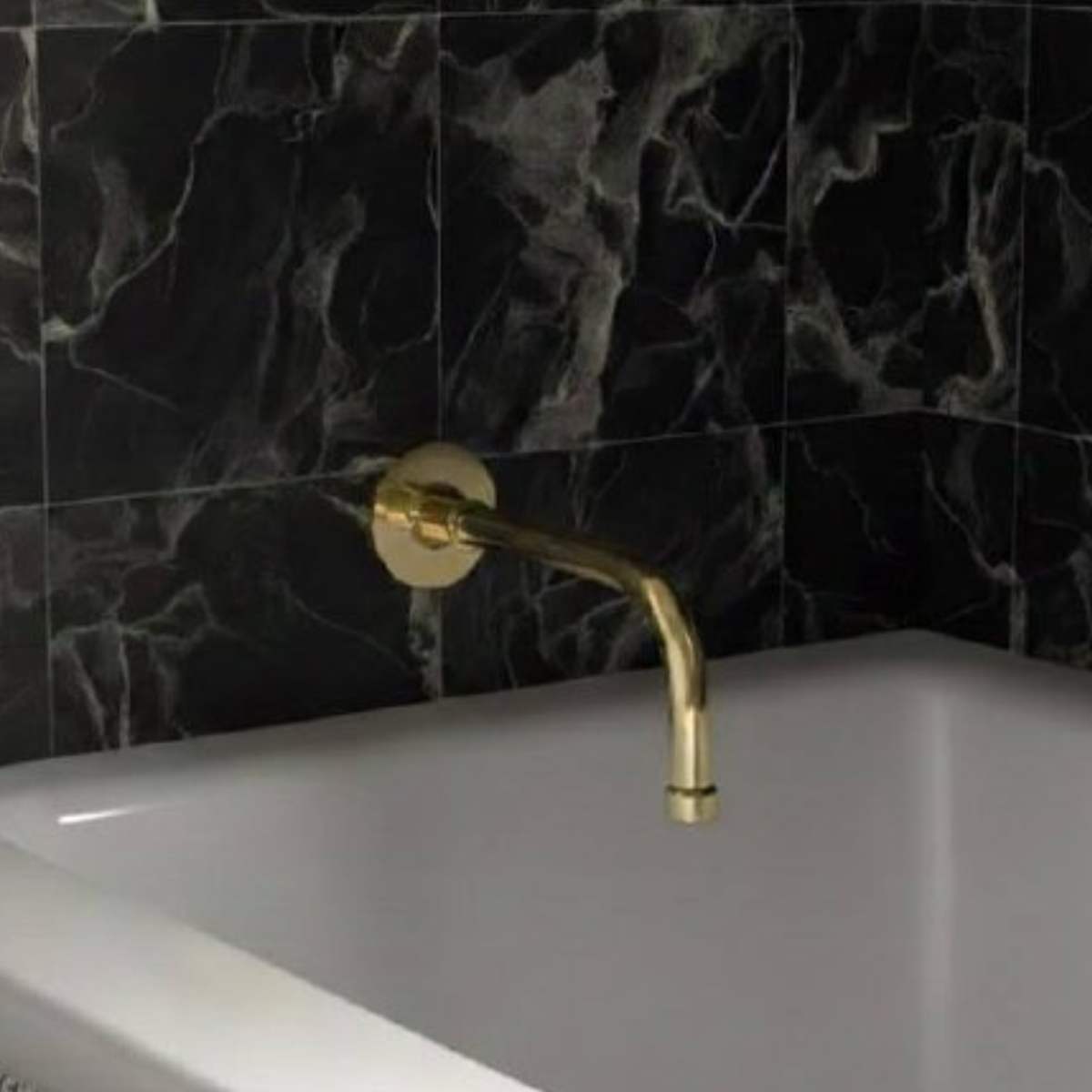Classic unlacquered brass wall-mount tub spout with curved neck installed above a white bathtub and black marble wall