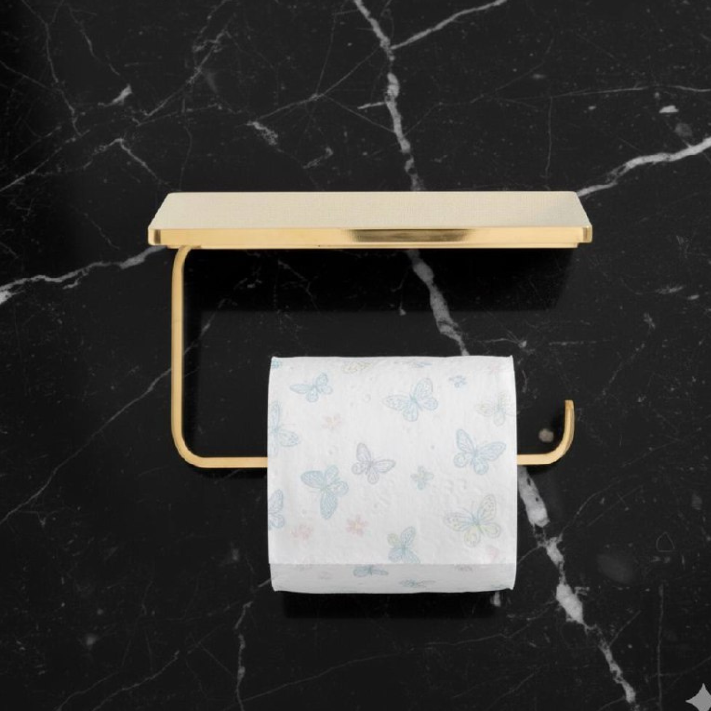 Wall-mounted unlacquered brass toilet roll holder with shelf, holding a standard toilet paper roll in a vintage bathroom setting
