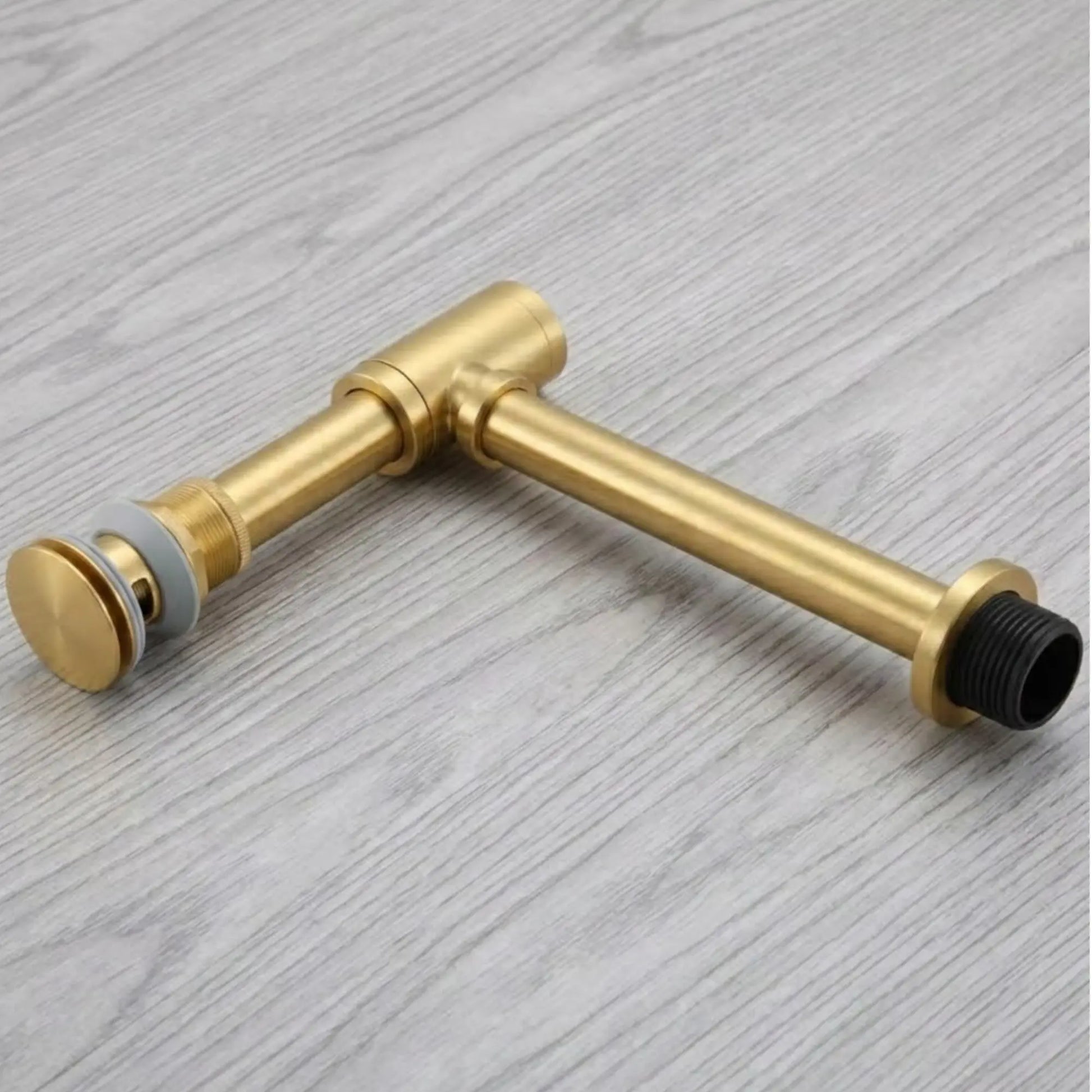 1-1/4 inch unlacquered brass bottle P-trap component flat lay showing threaded wall outlet, adjustable tailpiece, and pop-up drain cap detail