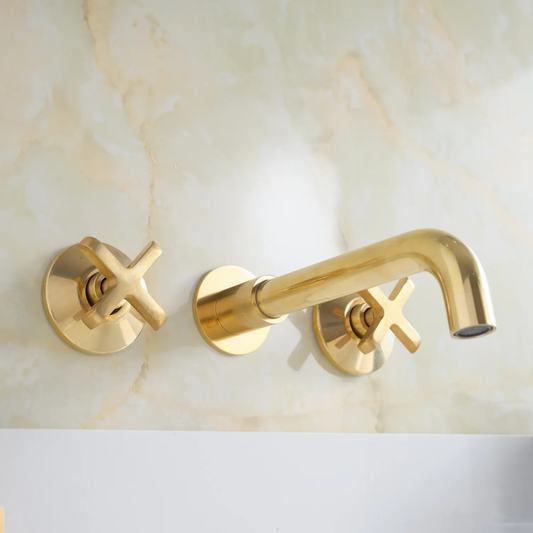 Unlacquered brass wall-mount bathroom faucet installed on sink, solid brass construction with living finish and vintage cross handles