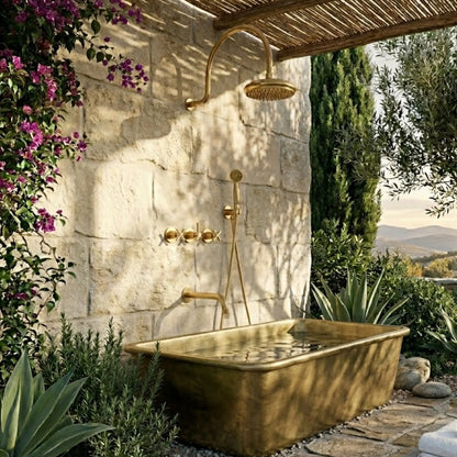 Unlacquered brass outdoor shower system and matching rectangular solid brass bathtub on a luxury stone patio.
