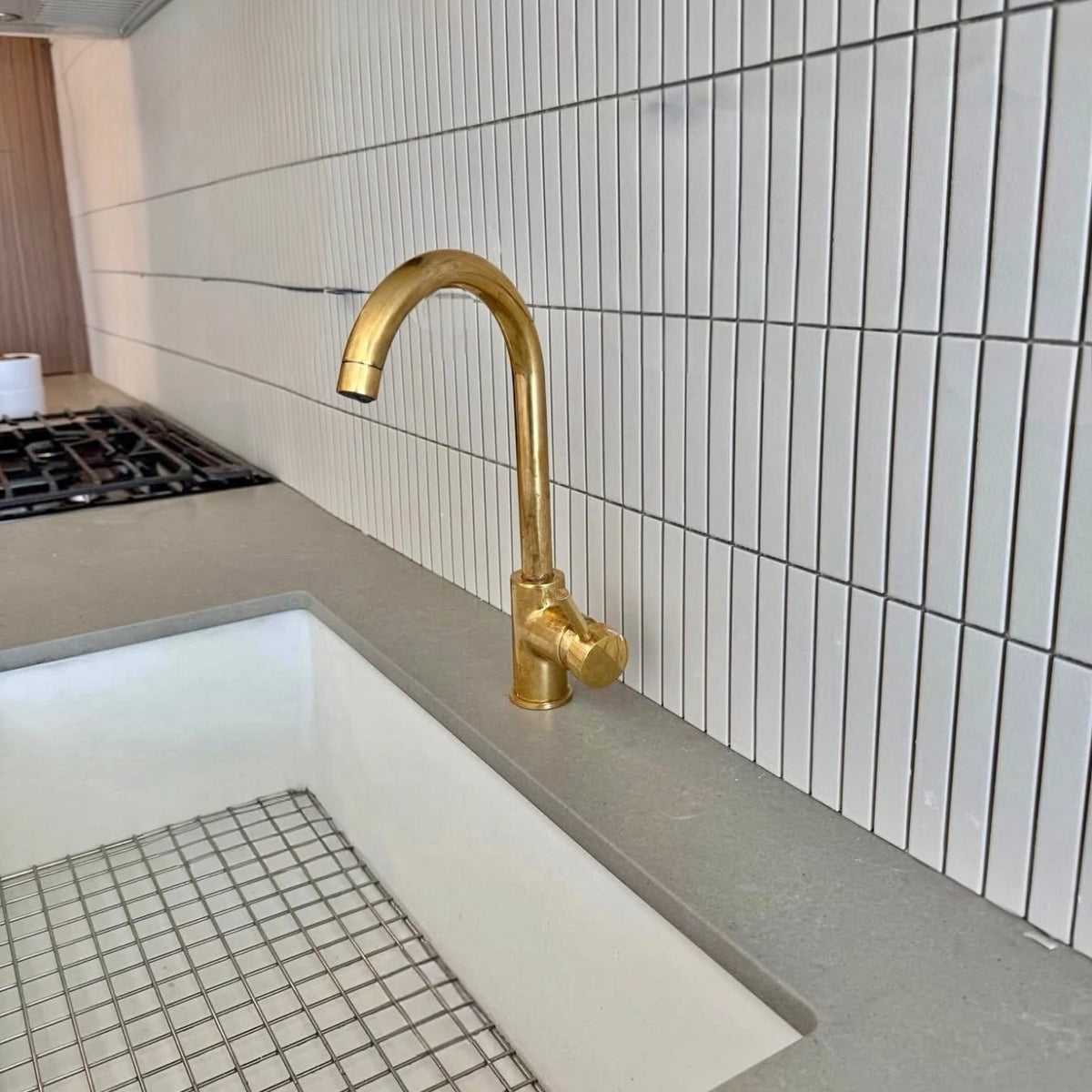 Gold faucet on a kitchen sink with tiled wall in the background