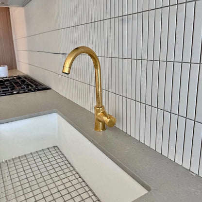 Gold faucet on a kitchen sink with tiled wall in the background