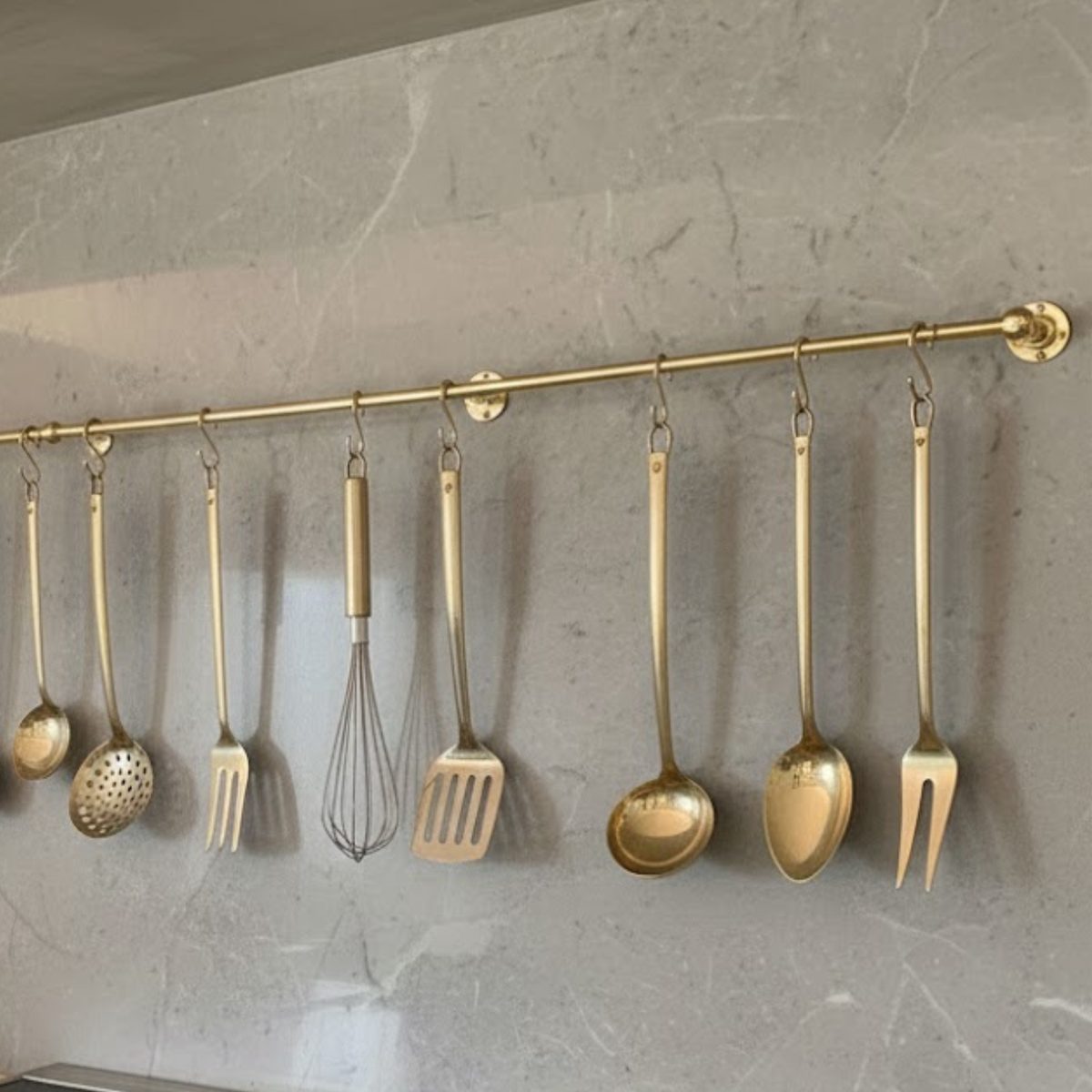Solid brass kitchen hanging rail mounted on stone wall with cooking utensils and tools