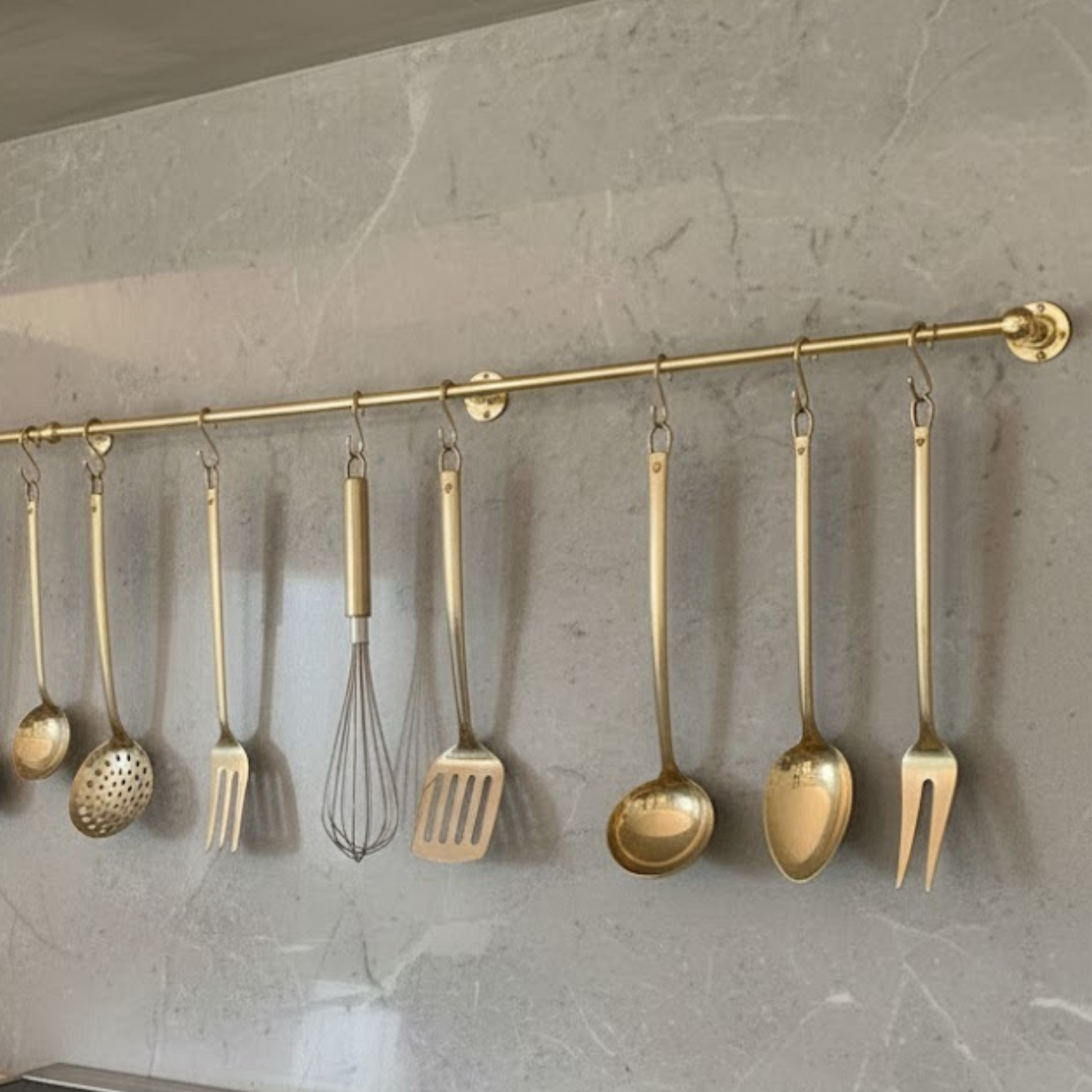 Solid brass kitchen hanging rail mounted on stone wall with cooking utensils and tools