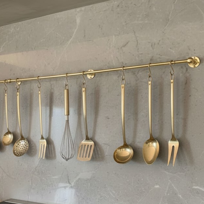 Solid brass kitchen hanging rail mounted on stone wall with cooking utensils and tools