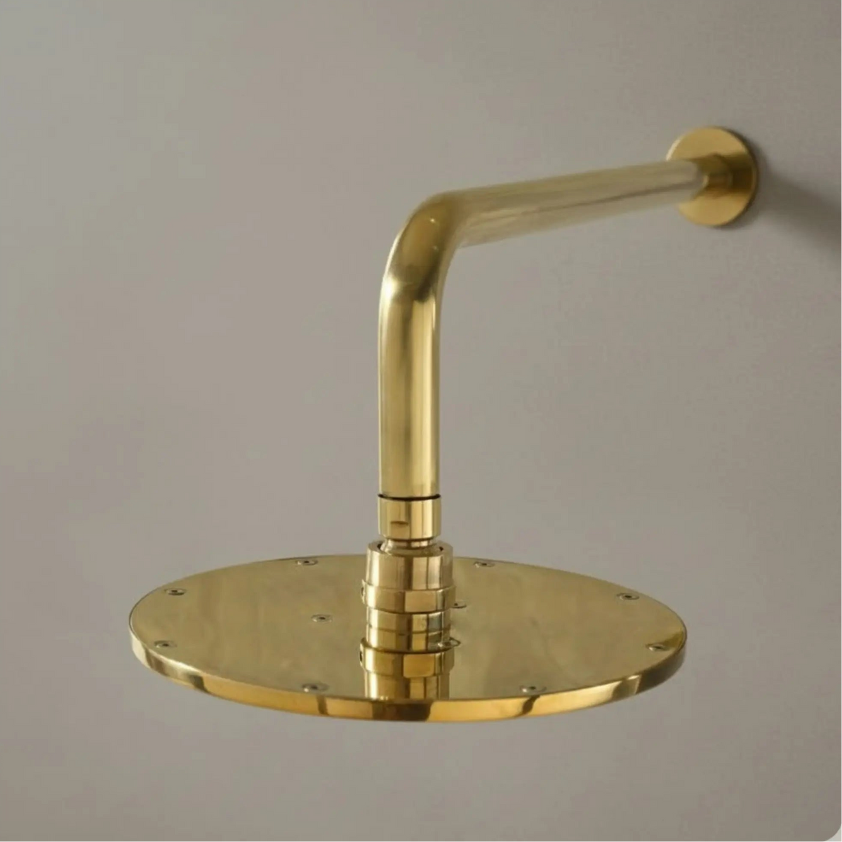 Close-up side profile of the solid brass shower arm and round rainfall head against a gray wall.