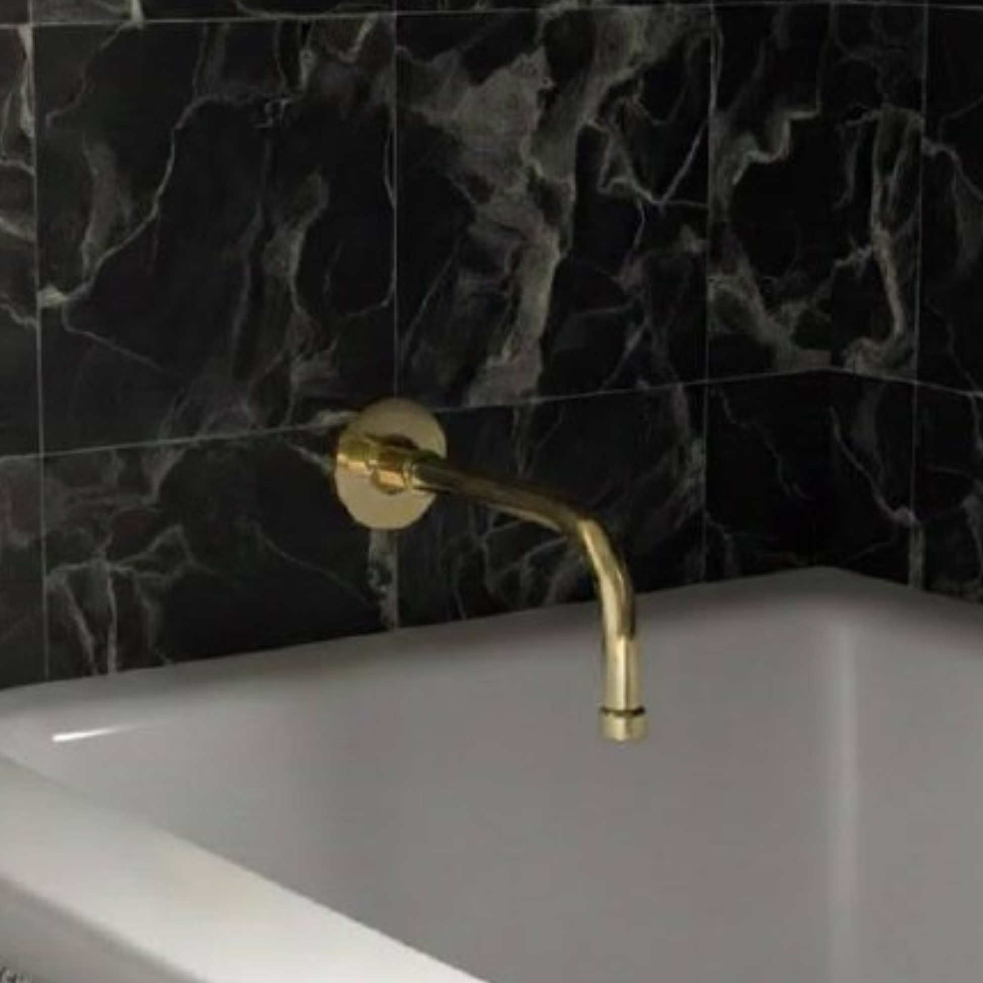 Classic unlacquered brass wall-mount tub spout with curved neck installed above a white bathtub and black marble wall