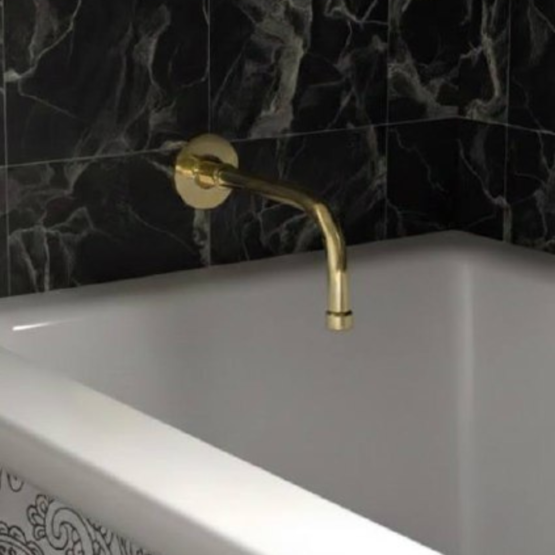 Unlacquered brass wall-mounted tub spout with curved design above a white bathtub against black marble tiles