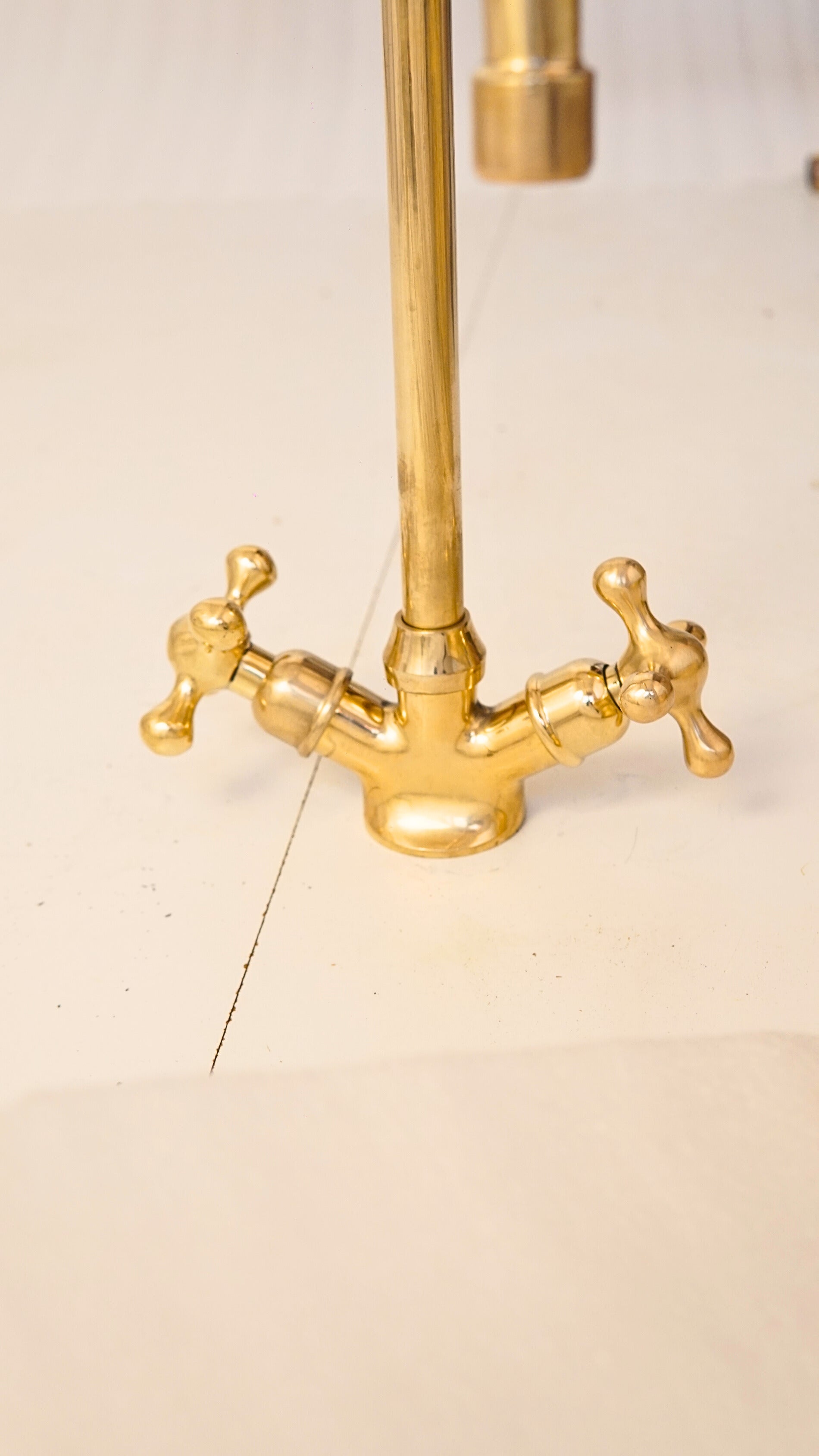 Close-up of double cross handles on a solid unlacquered brass basin faucet, showing classic vintage design and precision control.