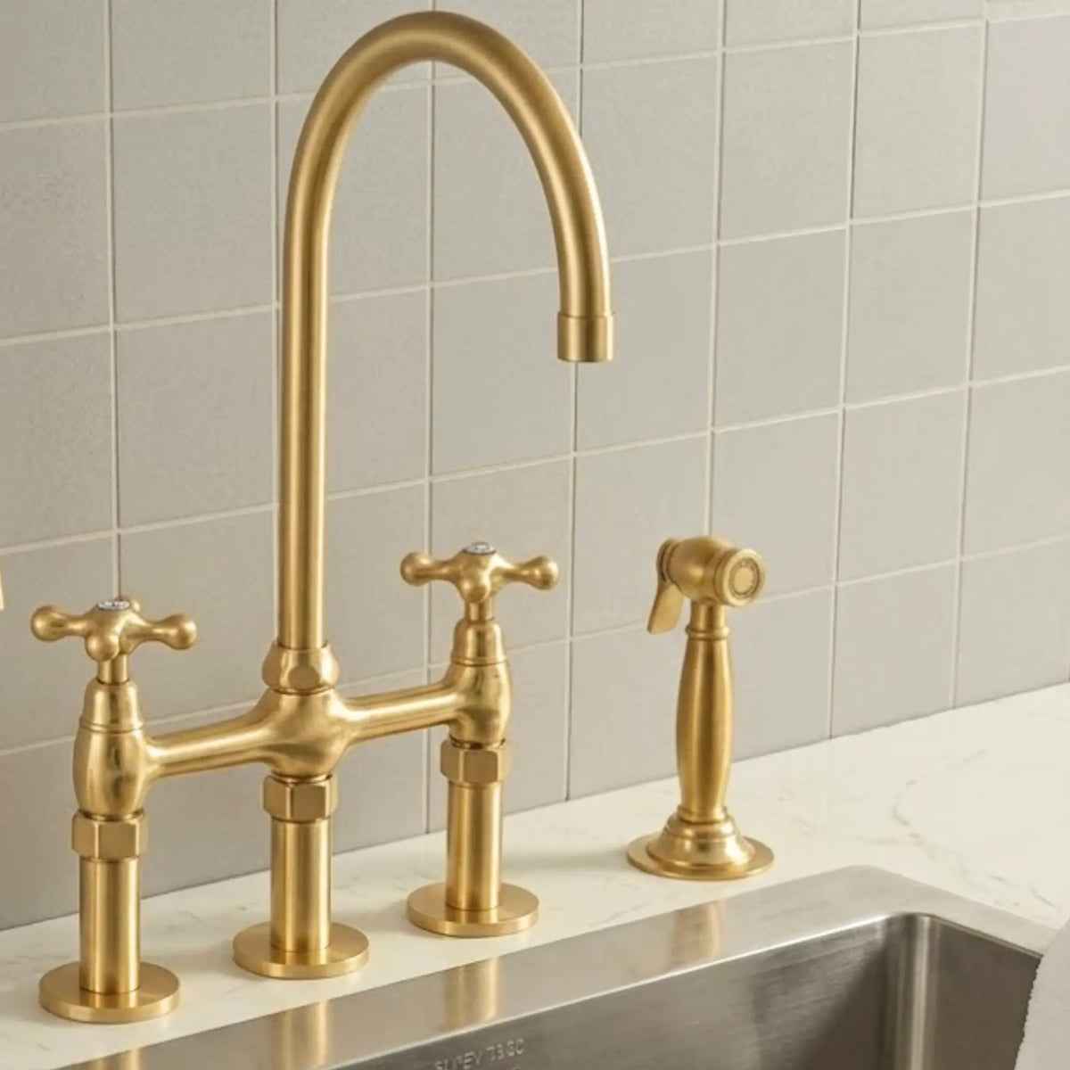 A three-hole bridge faucet set in brushed gold brass, featuring a high-arc main spout, two cross-handle hot and cold valves, and a matching side spray nozzle, installed on a white marble countertop against a light gray tiled backsplash.
