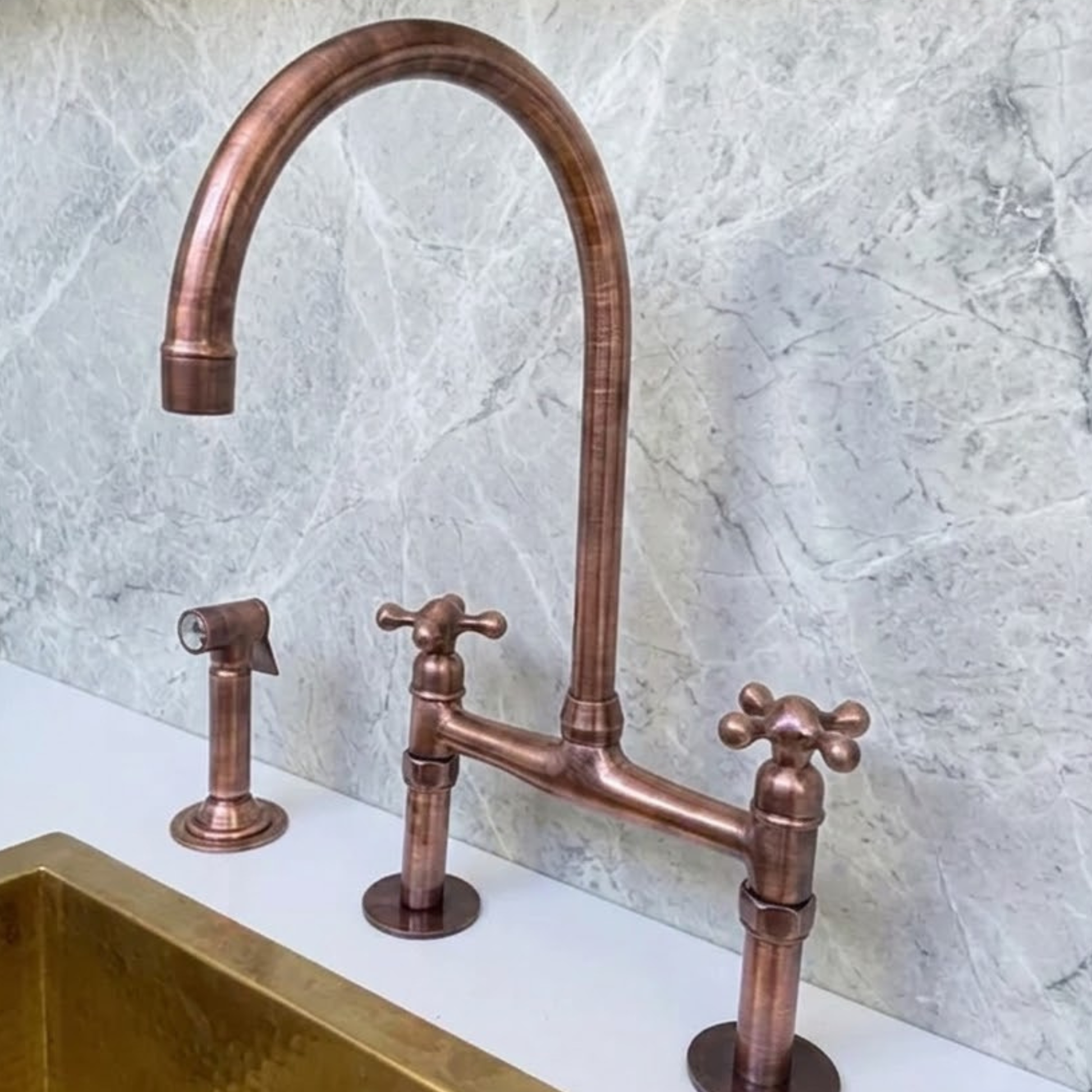 Solid copper bridge kitchen faucet with cross handles and side sprayer installed above brass farmhouse sink