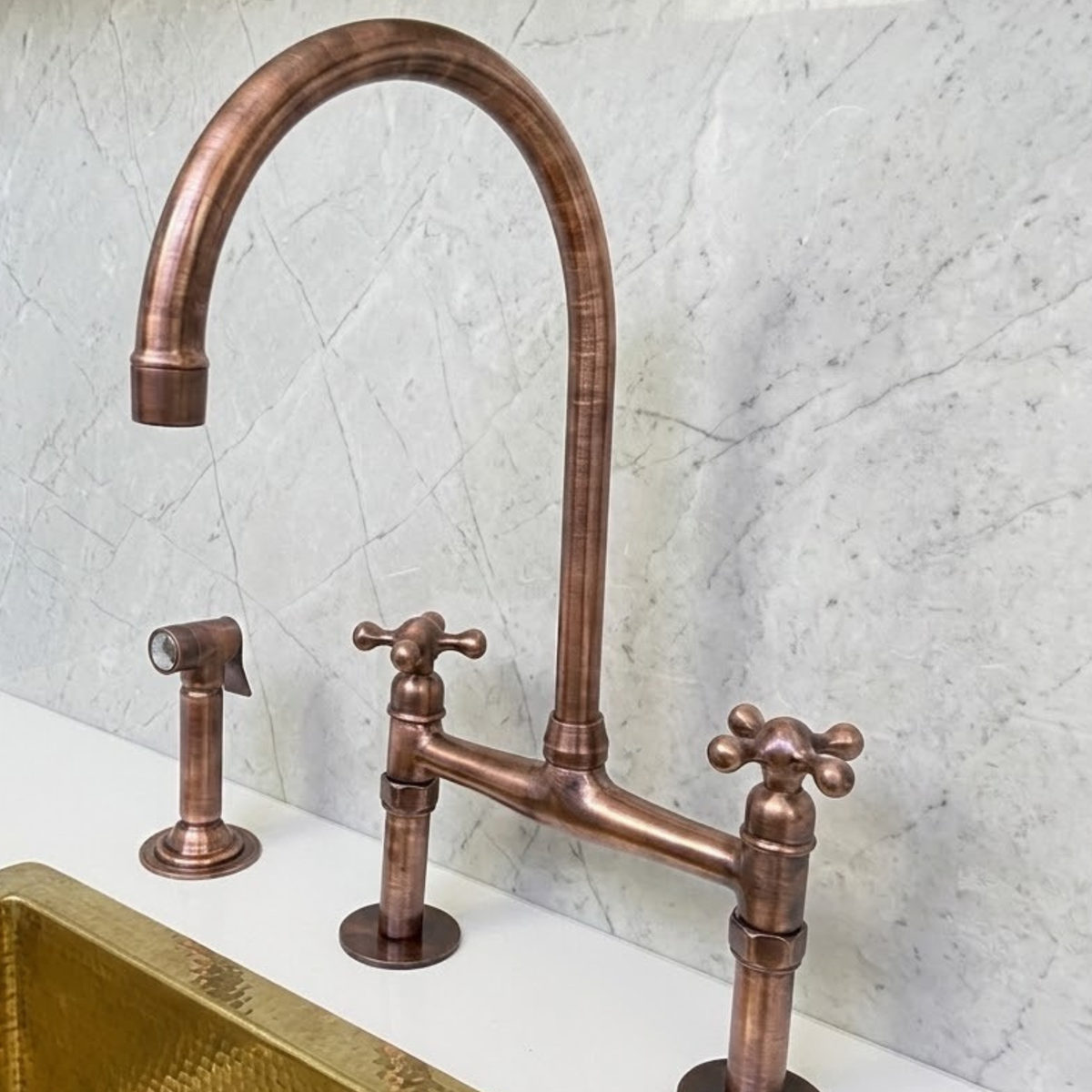 Solid copper bridge kitchen faucet with side sprayer and cross handles installed on farmhouse sink
