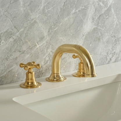 Luxury unlacquered brass 3-hole widespread bathroom faucet with cross handles mounted on a white vanity sink with light gray marble wall