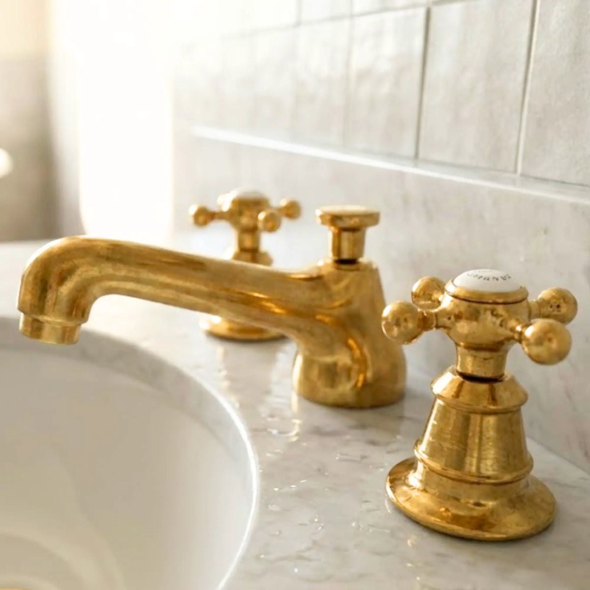 Solid unlacquered brass bathroom faucet with dual cross handles on marble vanity with ceramic tile backsplash