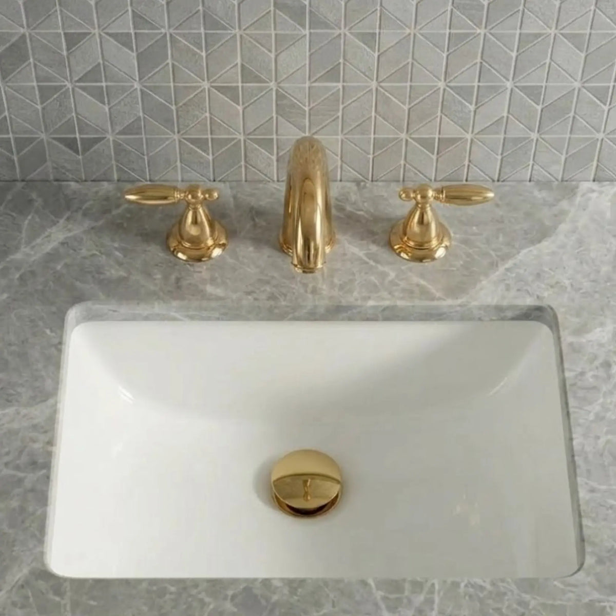 Sella unlacquered brass widespread bathroom faucet with cross handles and pop-up drain installed on white undermount sink with marble countertop