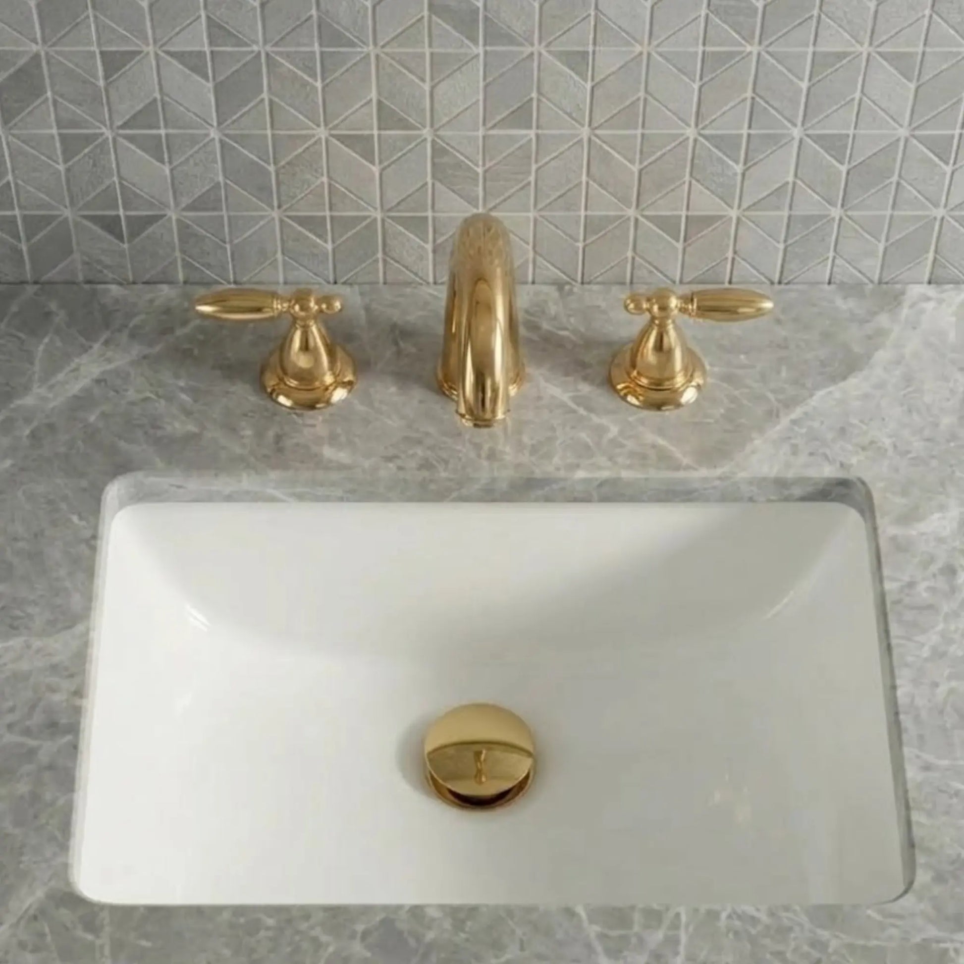 Sella unlacquered brass widespread bathroom faucet with cross handles and pop-up drain installed on white undermount sink with marble countertop