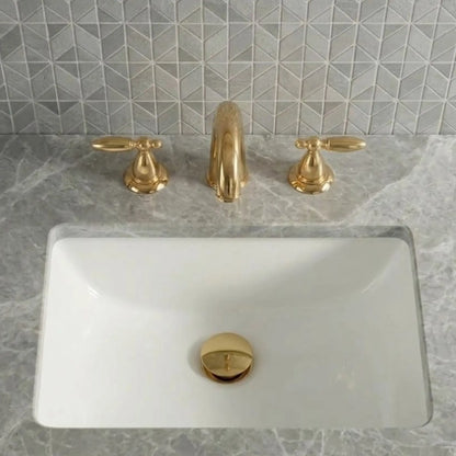 Sella unlacquered brass widespread bathroom faucet with cross handles and pop-up drain installed on white undermount sink with marble countertop
