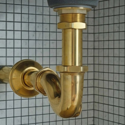 Bathroom sink P-trap drain pipe kit in solid brass installed under ceramic basin with tiled wall background