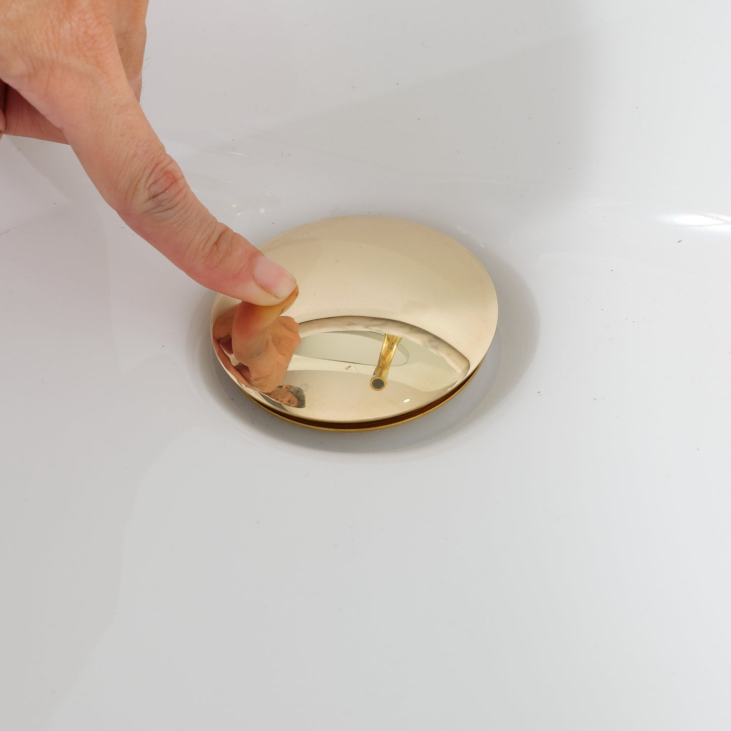Hand pressing an unlacquered brass pop-up sink drain demonstrating one-touch push-button operation