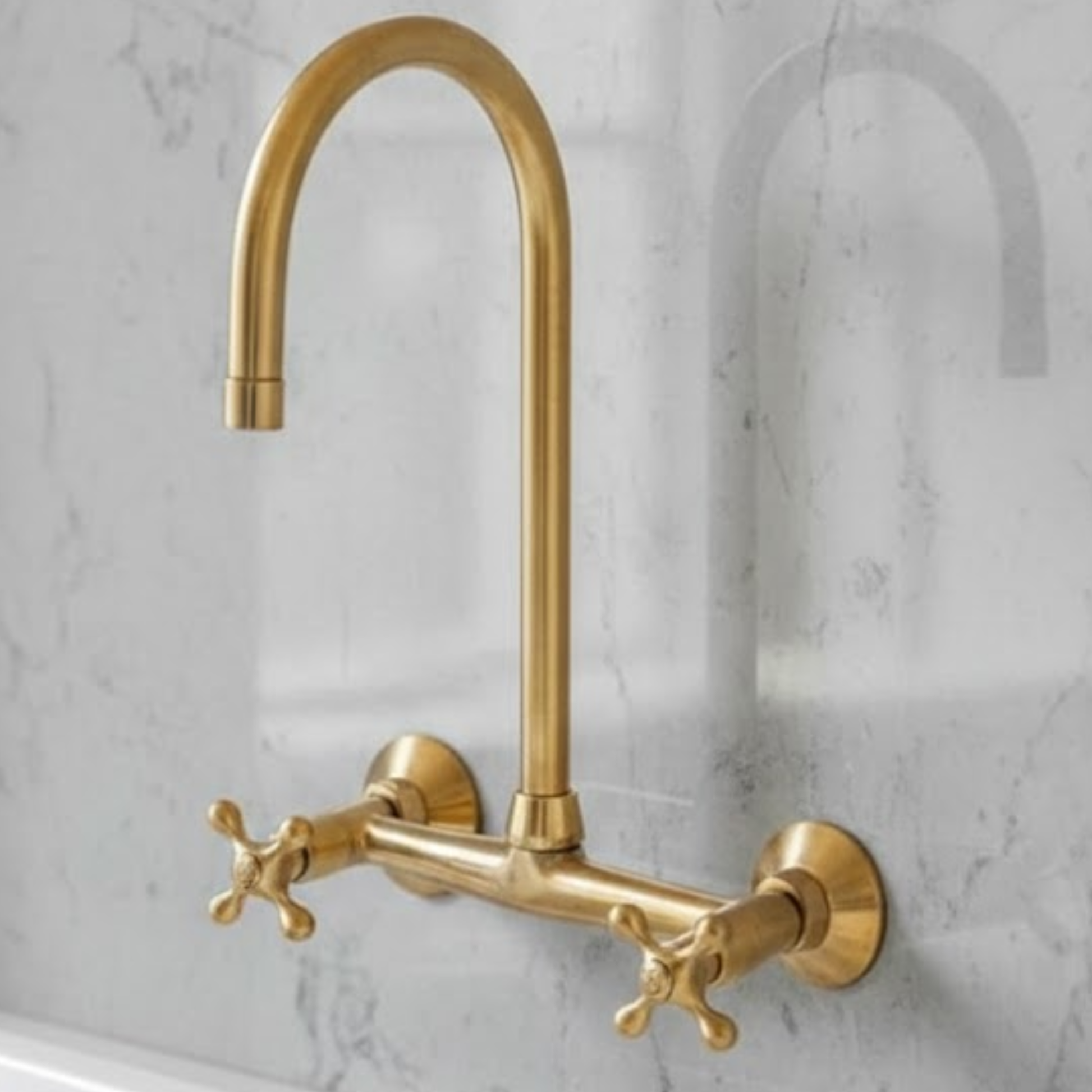 Ramsey wall-mounted unlacquered brass kitchen faucet with high-arc spout and cross handles installed on marble backsplash