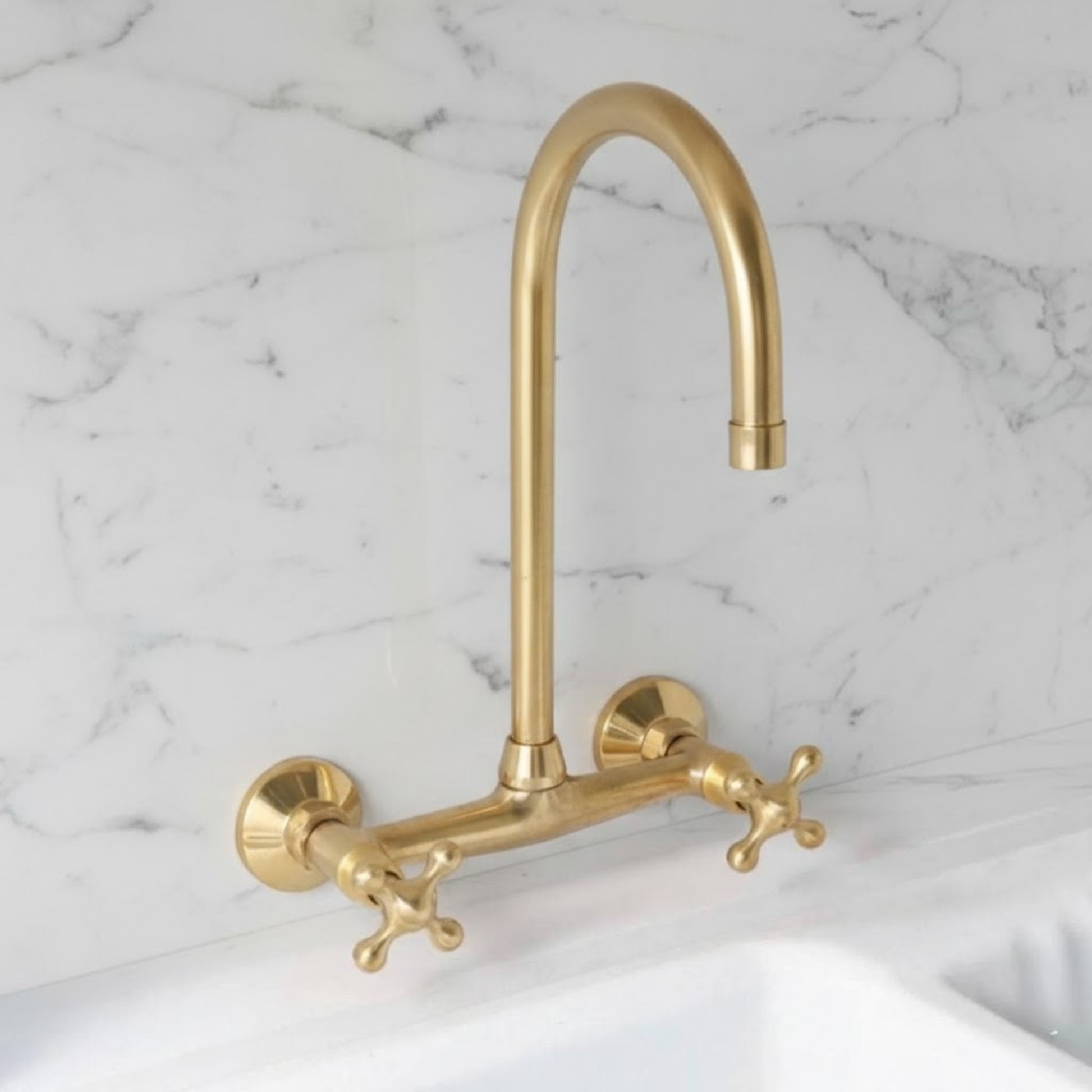 Ramsey wall-mounted kitchen faucet in unlacquered solid brass with cross handles installed on white marble backsplash