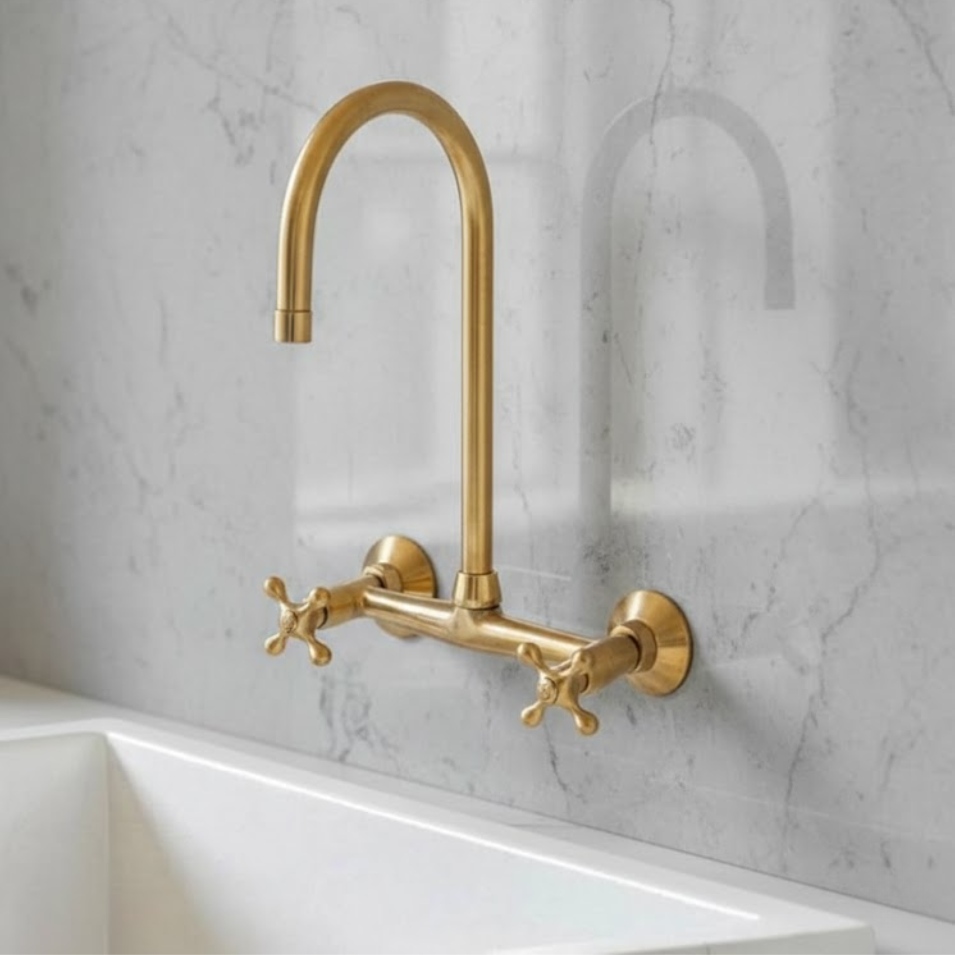 Unlacquered brass wall-mounted bridge kitchen faucet with cross handles installed on marble backsplash – Ramsey solid brass living finish