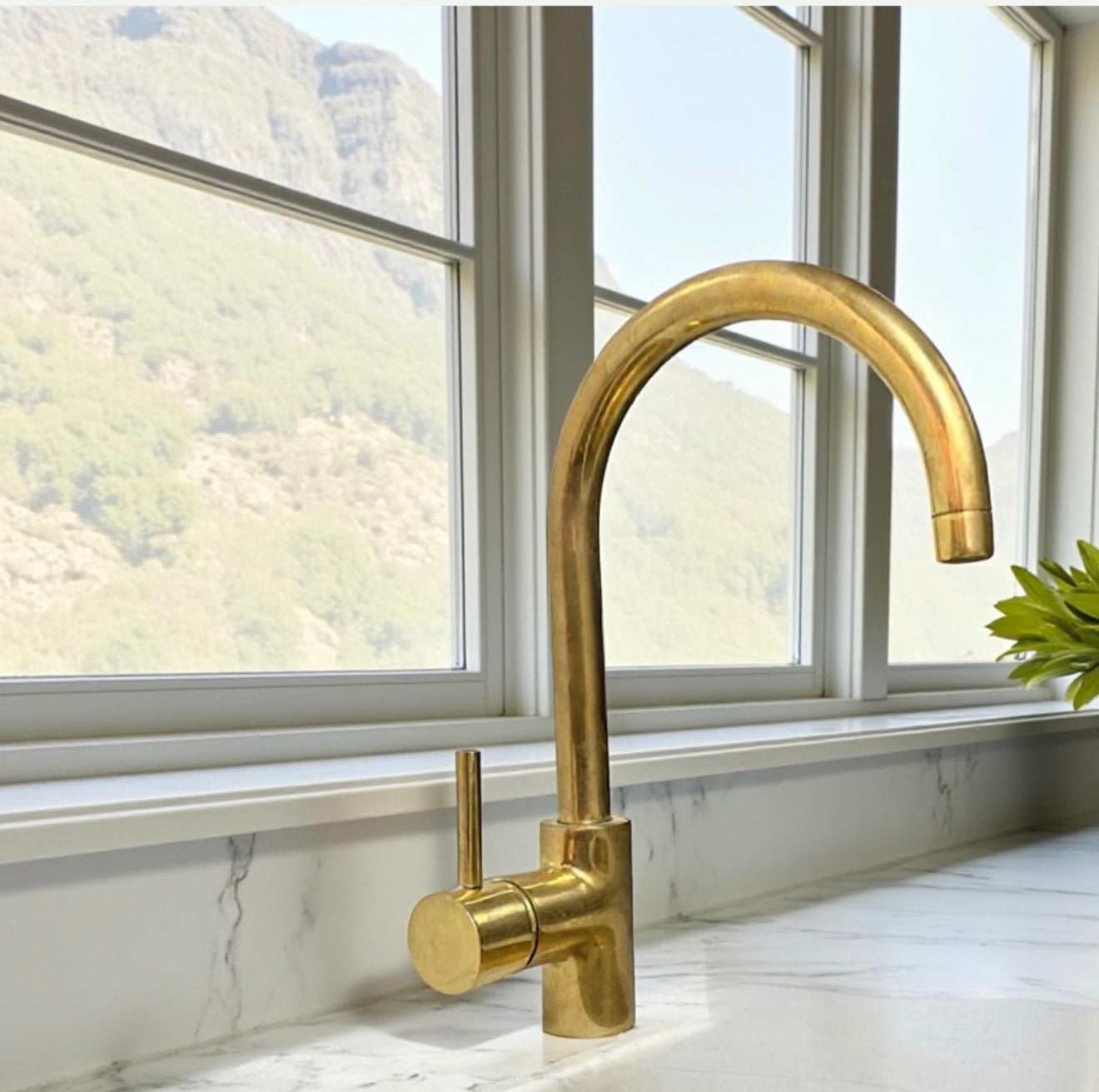 Gold kitchen faucet on a marble countertop with a window view of mountains