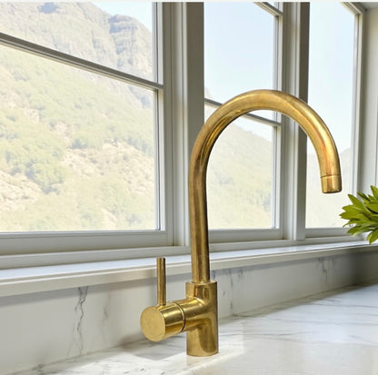 Gold kitchen faucet on a marble countertop with a window view of mountains