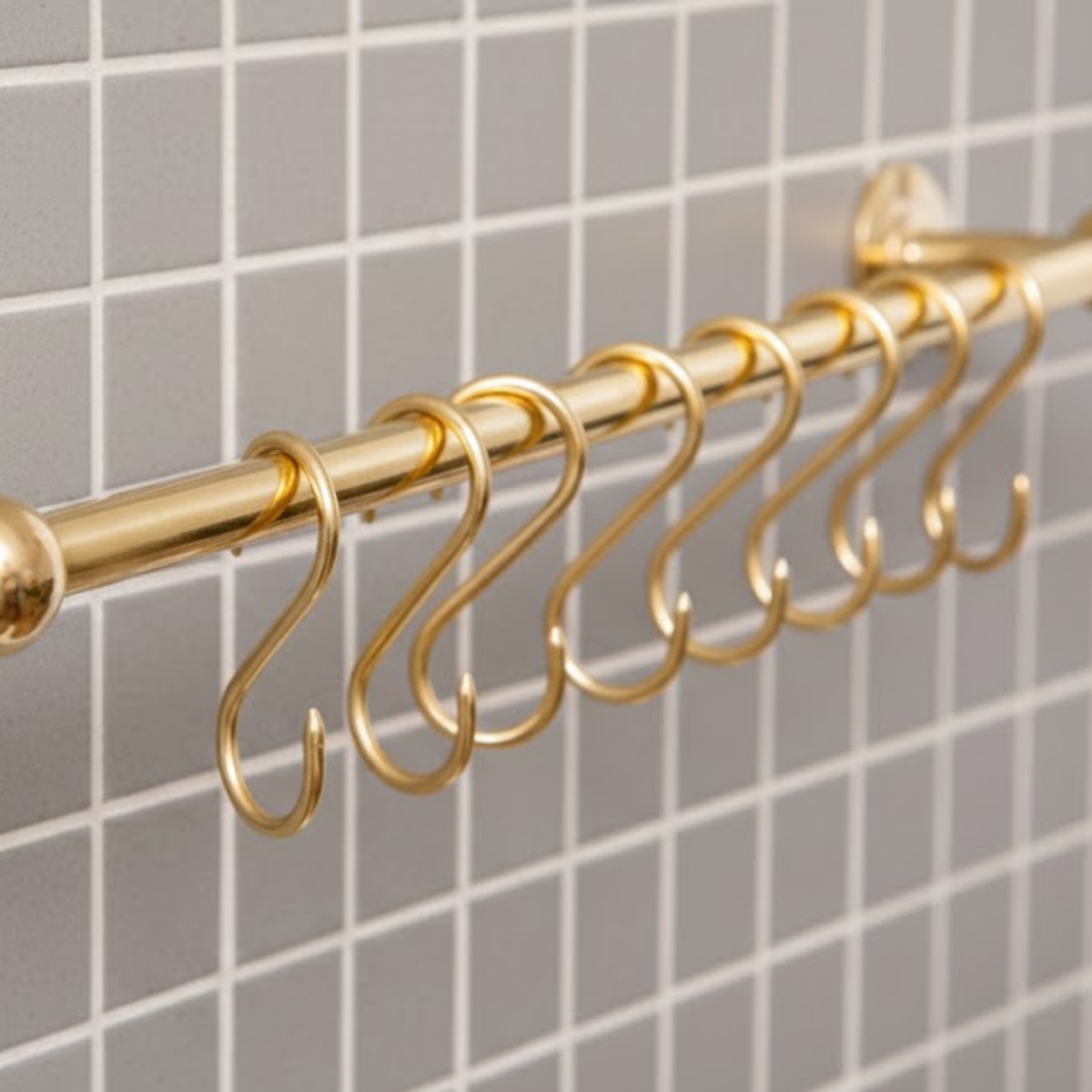 Close-up of solid brass S hooks hanging on unlacquered brass kitchen pot rail