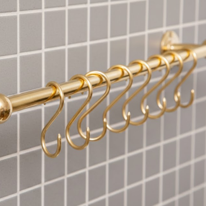 Close-up of solid brass S hooks hanging on unlacquered brass kitchen pot rail