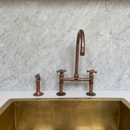 Copper kitchen faucet and sink against a marble wall.