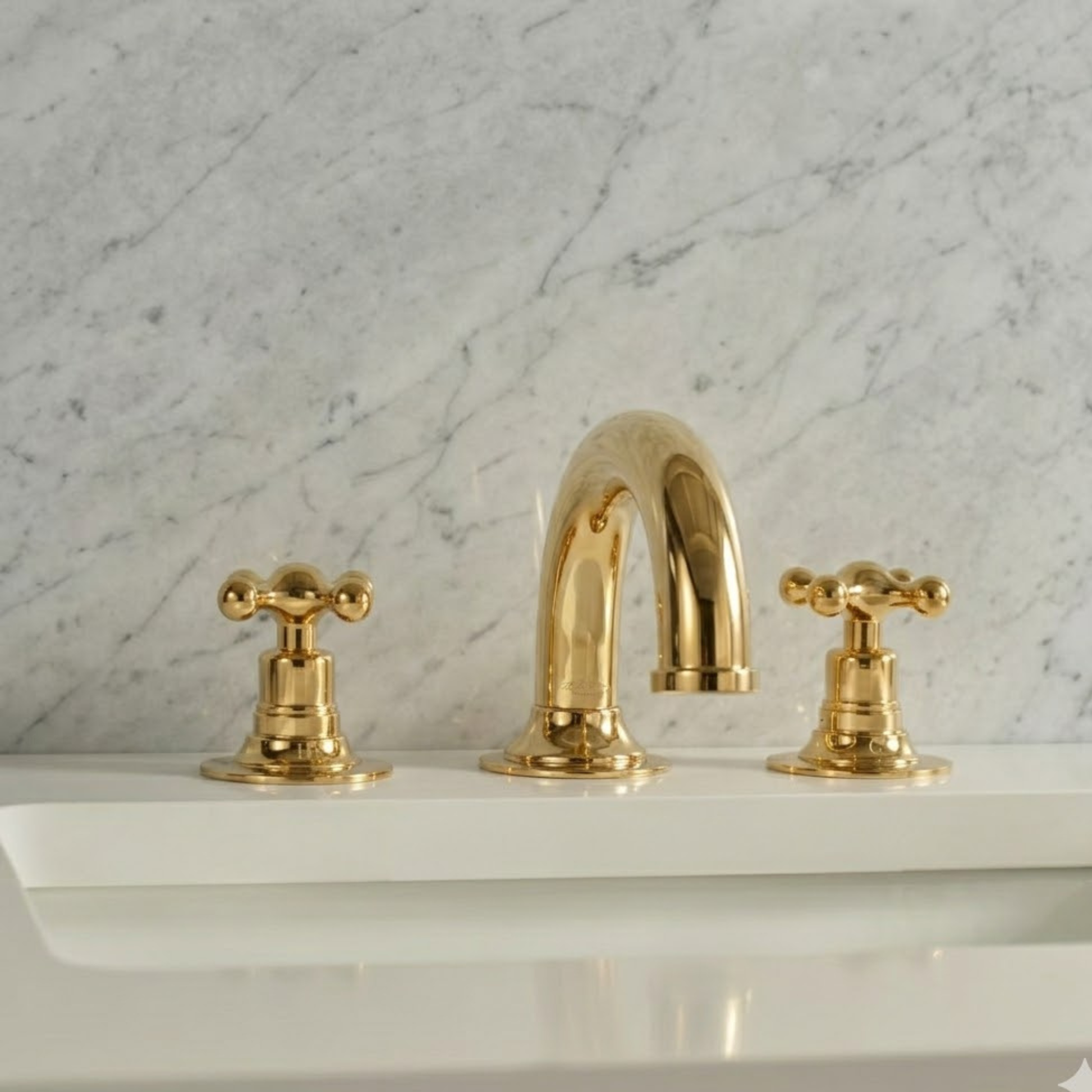 Unlacquered brass widespread bathroom faucet with cross handles installed on a white sink against a white marble wall