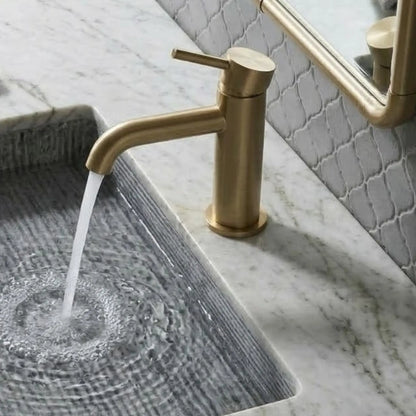 High-angle view of an unlacquered brass bathroom faucet on a white marble countertop with a gray fluted integrated sink and flowing water.
