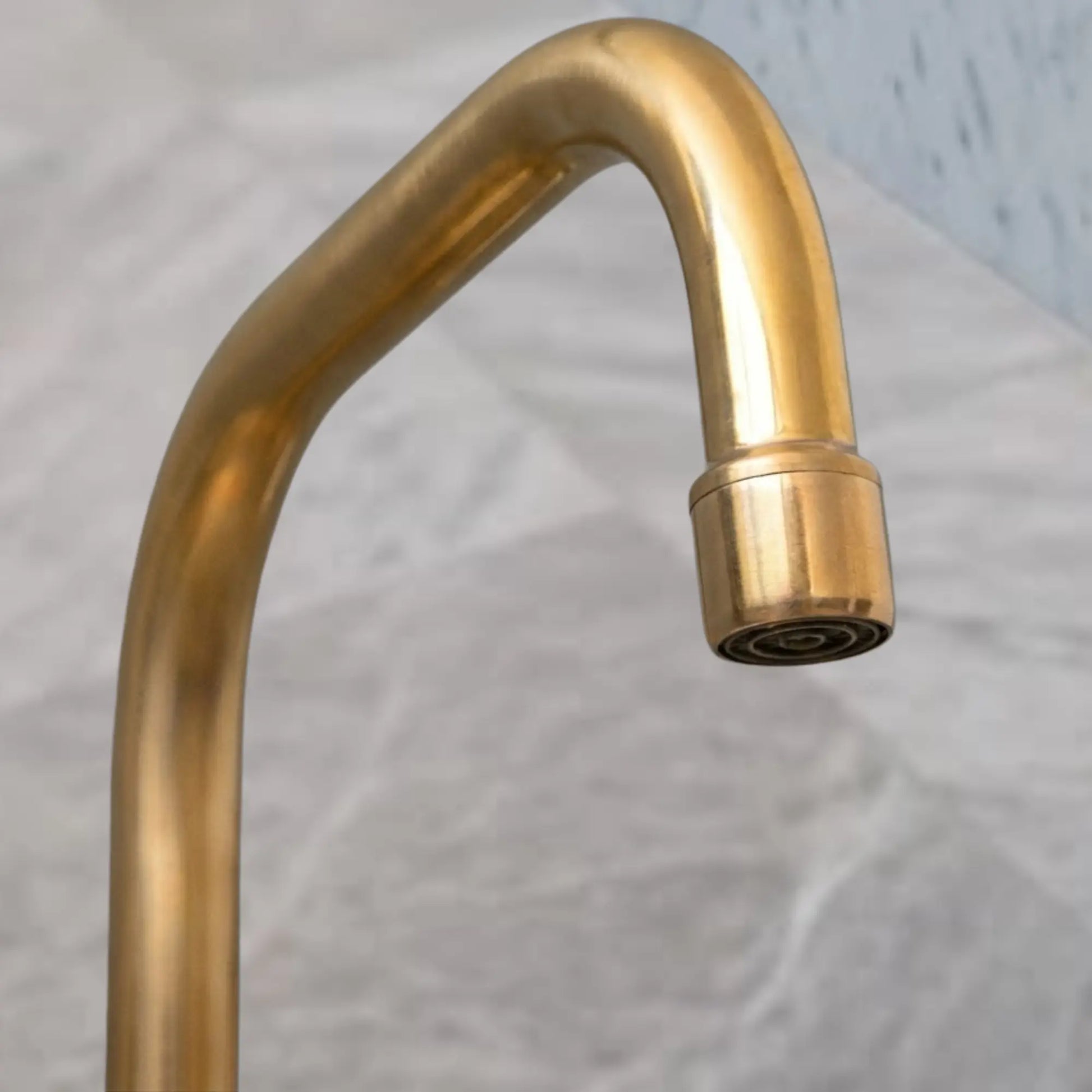 Unlacquered brass faucet spout close-up showing natural patina finish and aerator tip, gooseneck curve detail