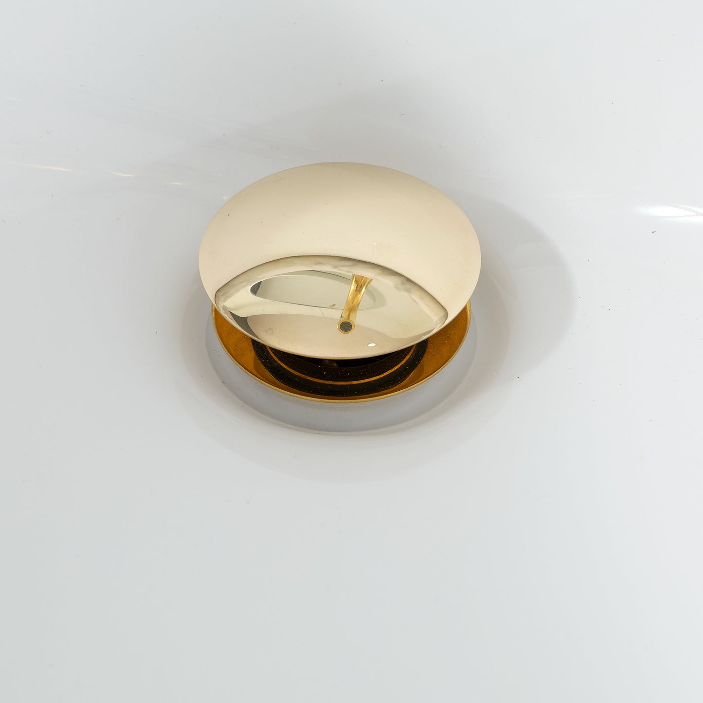 Top view of unlacquered brass pop-up drain stopper with smooth push-button mechanism