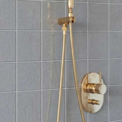 Close-up of unlacquered brass shower valve control and handheld shower hose installed on gray tiled bathroom wall