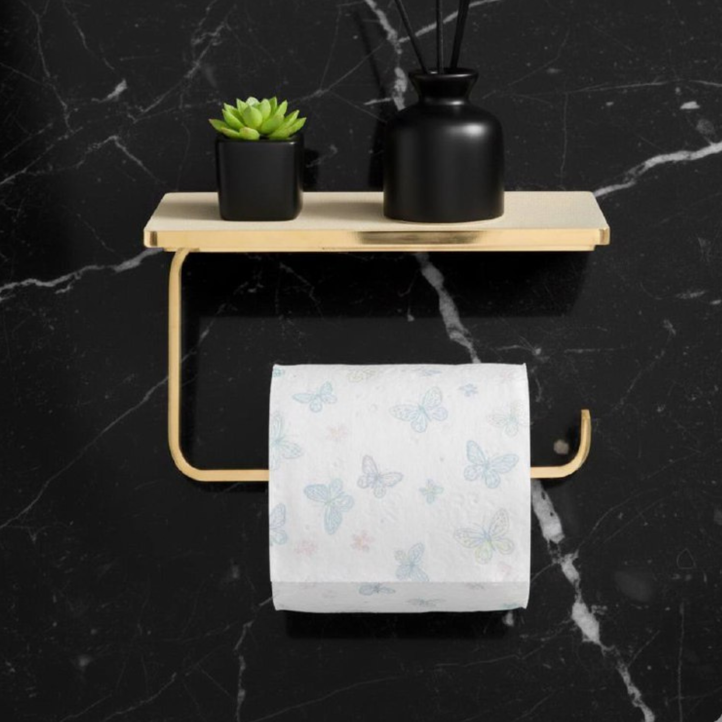 Unlacquered brass toilet paper holder with integrated shelf, mounted on a black marble wall in a vintage bathroom