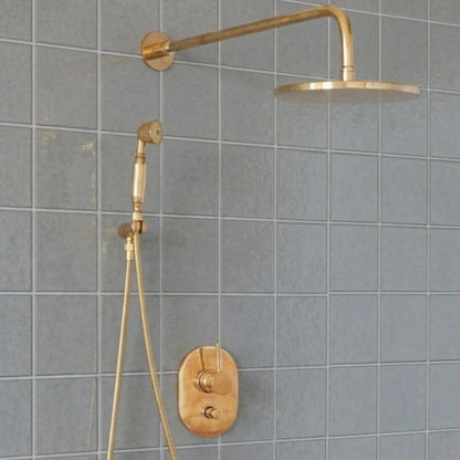 Unlacquered brass wall mount rain shower system with handheld shower and exposed pipe design installed on gray tiled bathroom wall