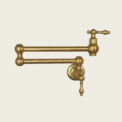 A wall-mounted double-jointed pot filler faucet in unlacquered brass finish with a traditional lever handle design, isolated on a light cream background.