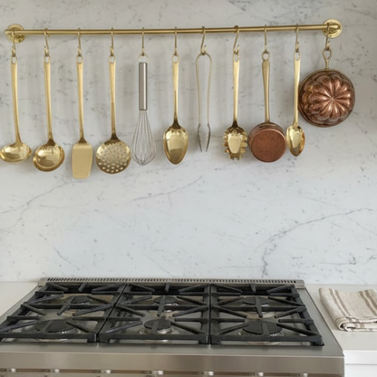 Unlacquered brass wall mounted pot rail installed above stove with hanging kitchen utensils