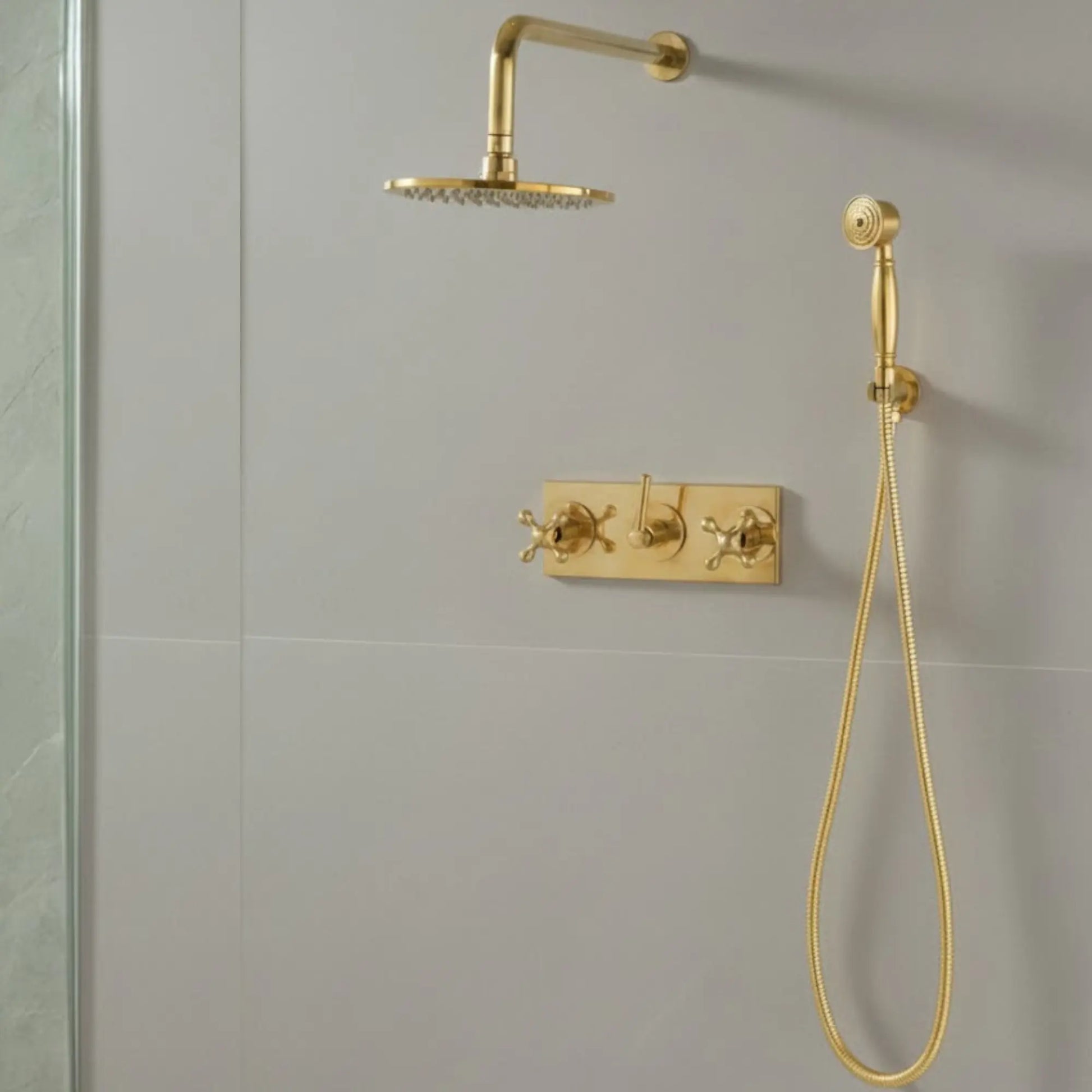 Main view of a vintage unlacquered brass wall-mounted shower system with a round rainfall head, handheld sprayer, and matching triple cross-handle controls