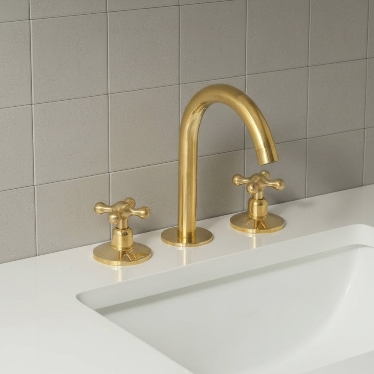 Brass faucet and handles on a white sink with gray tiled wall background