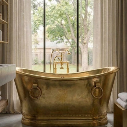 A freestanding brass bathtub with matching vintage-style faucet, placed in front of large windows with curtains and a garden view.