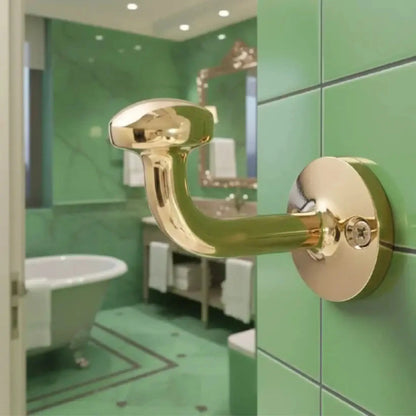 Unlacquered solid brass wall hook installed in a bathroom interior, blending classic design with modern green ceramic tiles.