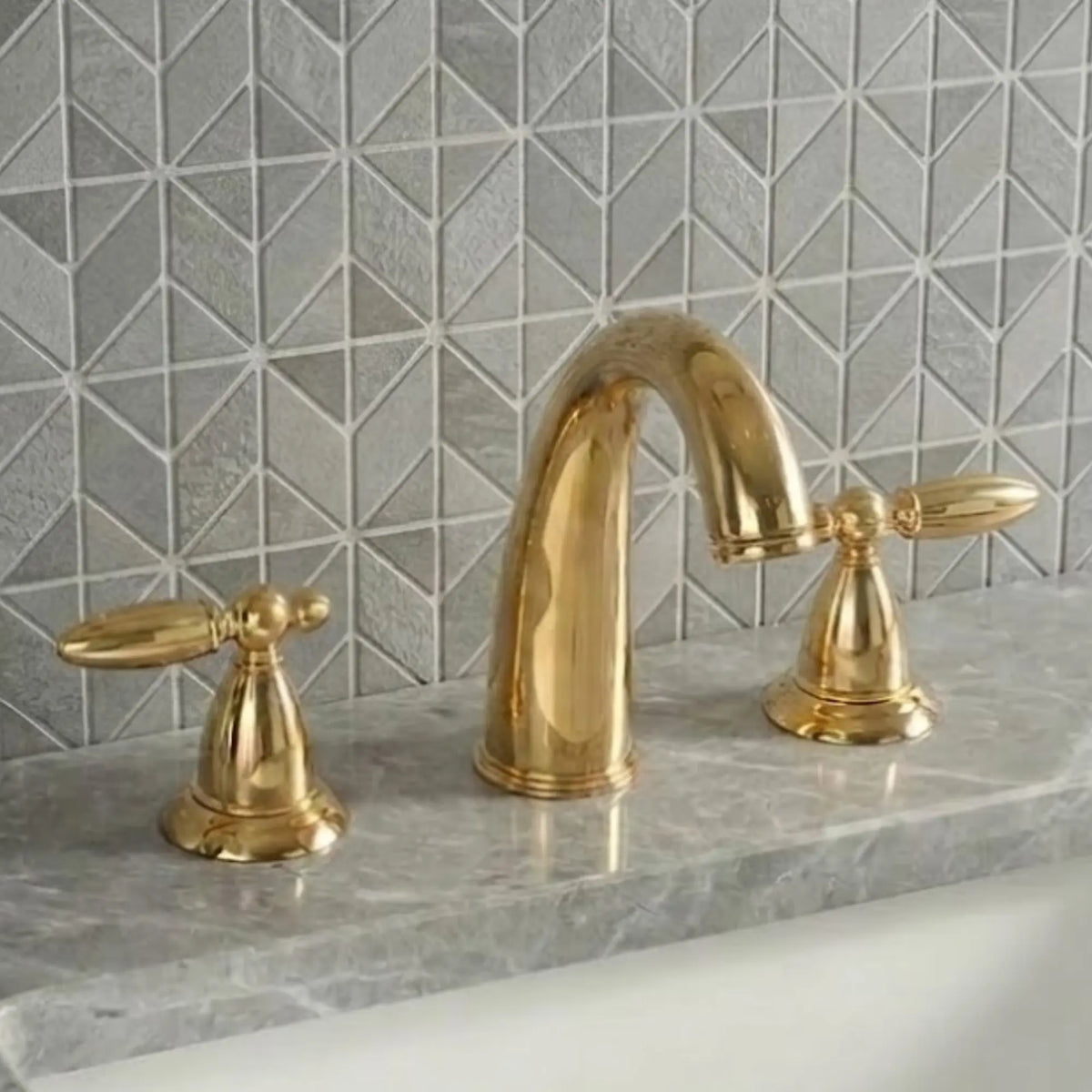 Sella unlacquered brass widespread bathroom faucet front view with polished high-arc gooseneck spout and symmetrical cross handles on gray marble countertop