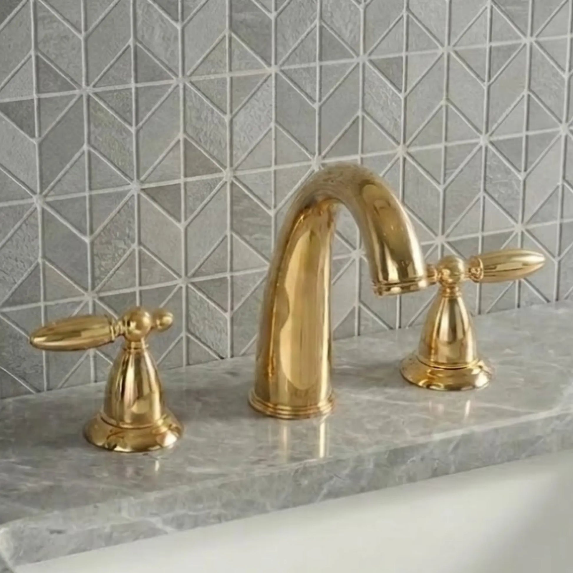 Sella unlacquered brass widespread bathroom faucet front view with polished high-arc gooseneck spout and symmetrical cross handles on gray marble countertop