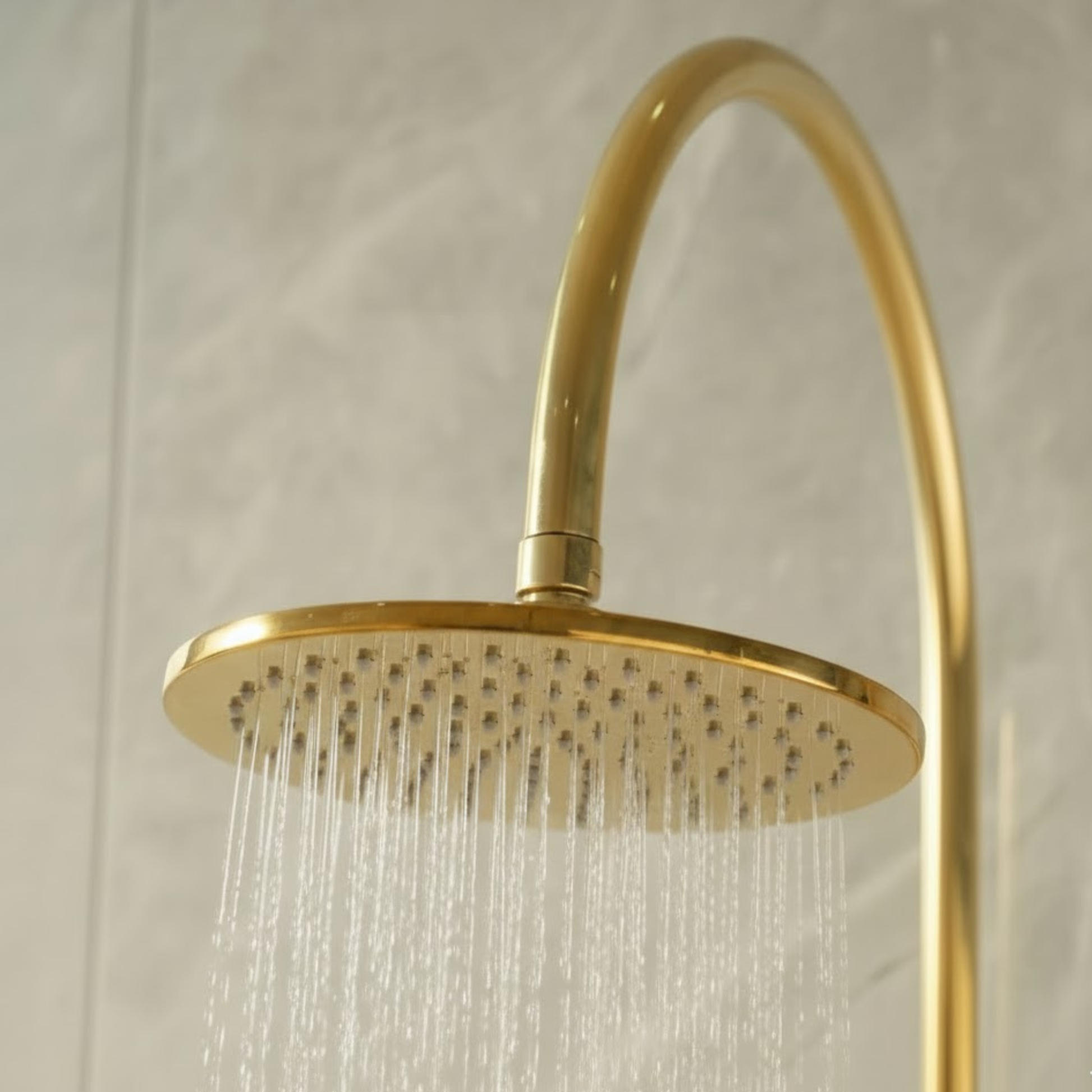 Close-up of the luxury unlacquered brass rainfall shower head with water flowing, showcasing the spray pattern.