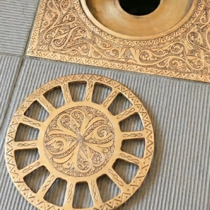 Disassembled unlacquered brass square floor drain showing removable engraved circular grate and drain body