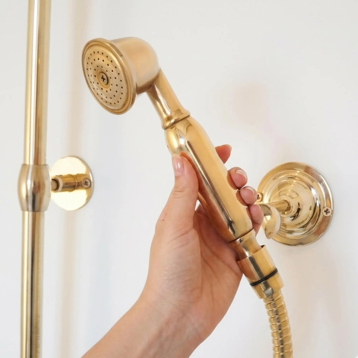 Hand holding BrassOna® unlacquered brass handheld shower sprayer — vintage solid brass hand shower with wall mount holder
